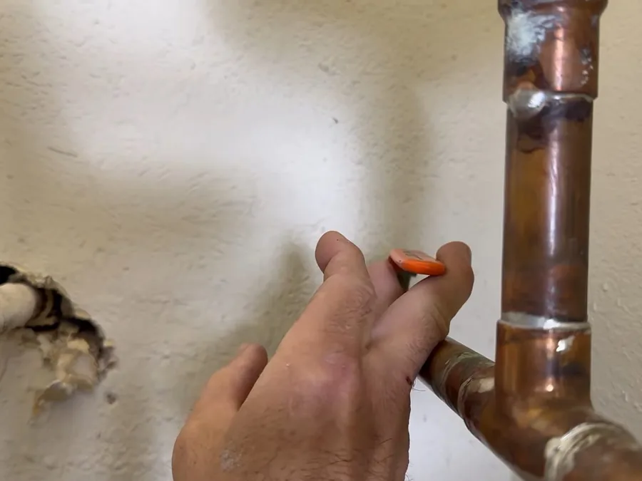 Technician checking a copper pipe near a wall opening during leak detection