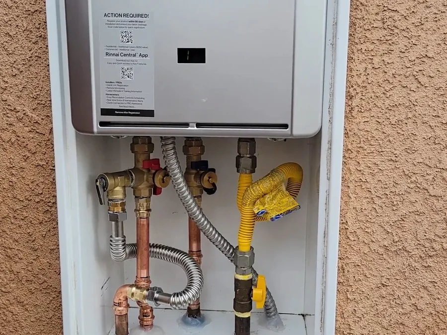 Exterior tankless water heater mounted with gas and water connections visible