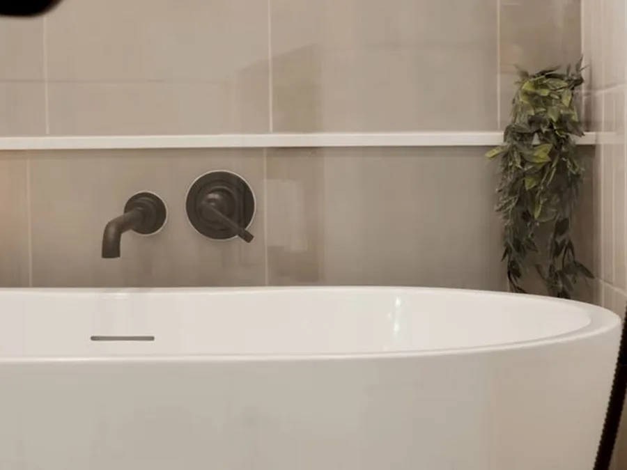 Freestanding bathtub with wall-mounted filler and finished tile surround