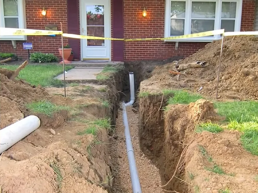 New white sewer pipe installed in a yard trench near a home